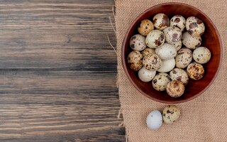 top view of quail eggs on a wooden bowl on sack cloth on a wooden background with copy space
