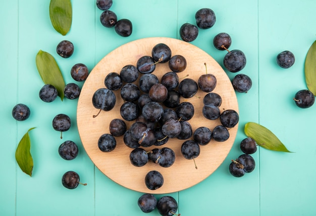 無料写真 青色の背景に木製キッチンボード上の小さな酸っぱい黒っぽい果物のスローのトップビュー