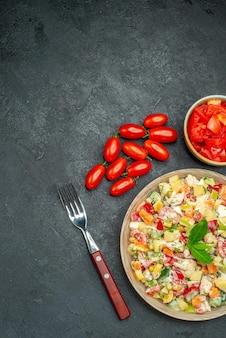 濃い灰色の背景にトマトとフォークの野菜サラダの上面図