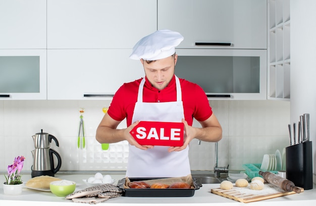 흰색 부엌에서 판매 사인을 보여주는 젊은 집중된 남성 요리사의 상위 뷰