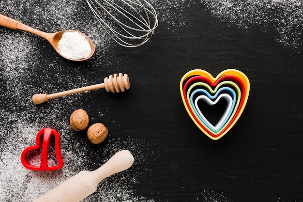 Top view ofcolorful heart shapes with kitchen utensils and flour