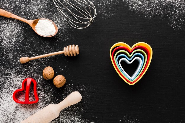 Top view ofcolorful heart shapes with kitchen utensils and flour