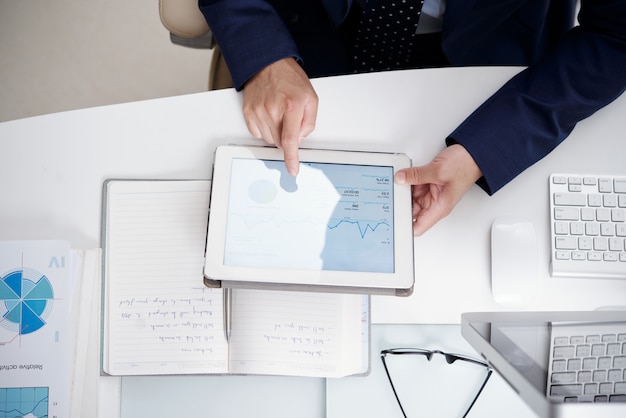 Top view of office desktop with notebook, documents, computer and digital tablet used by anonymous man