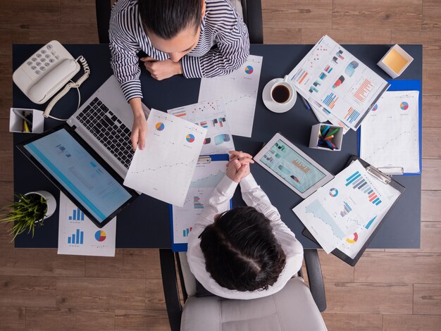 Top view of office workers meeting analyzing financial charts holding clipboard