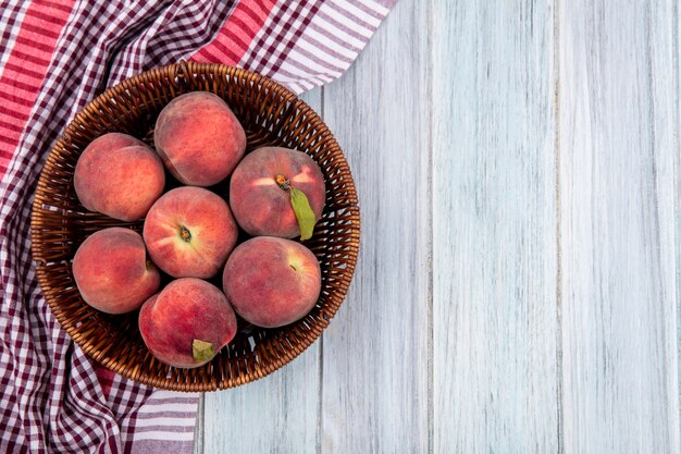 Top view offresh juicy and delicious peaches on a bucket on a checked tablecloth on grey wooden surface