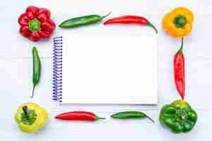 Free photo top view offul bell-peppers lined with spicy peppers and notepad on white, vegetable spice hot food meal product