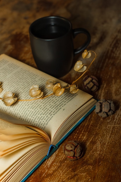 Top view an old book with coffee mug and dried flowers on wooden table. vertical