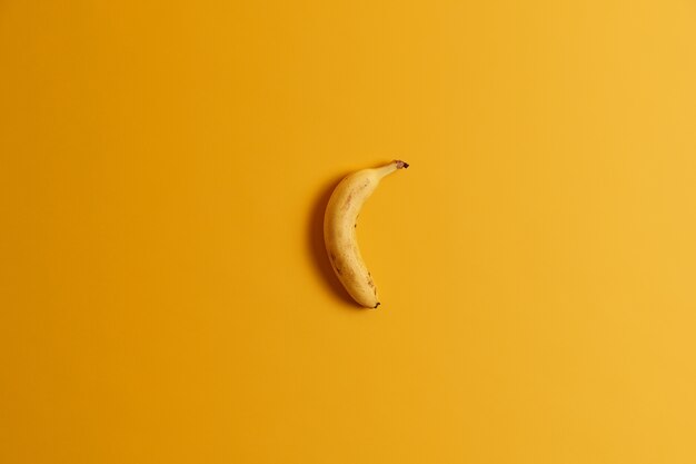黄色の背景の上に分離された1つの熟したバナナの上面図。あなたのおいしい朝食や軽食のためのおいしいトロピカルフルーツ。バナナを丸ごと食べる準備ができました。ビタミンが豊富な便利な栄養製品