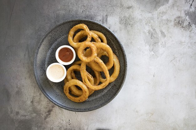 Top view of onion rings with different sauces in a plate on the table
