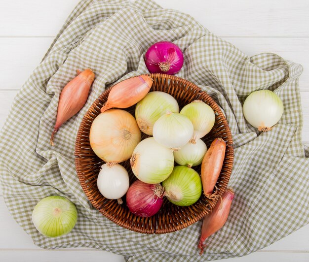 Top view of onions in basket on plaid cloth and on wooden background