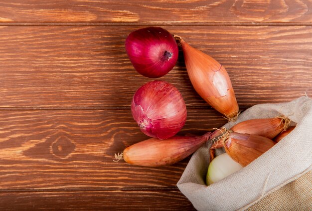 Top view of onions spilling out of sack on wooden background with copy space