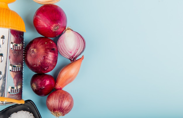 Top view of onions with salt and grater on left side and blue with copy space