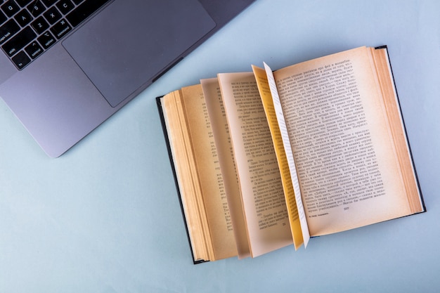 Free photo top view of an open book and laptop on blue