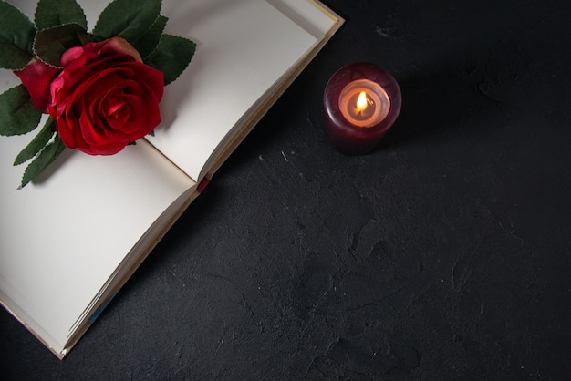 Free photo top view of open book with candle and red flower on dark wall