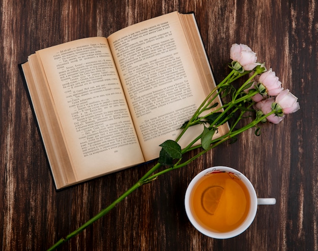 핑크 장미와 나무 표면에 차 한잔과 책의 상위 뷰