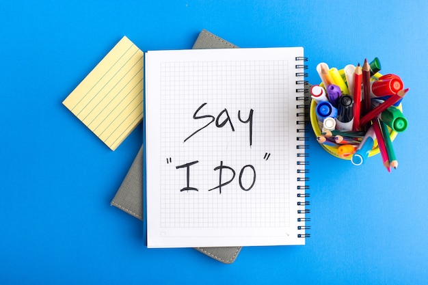 Free photo top view open copybook with felt pens and colorful pencils on blue desk