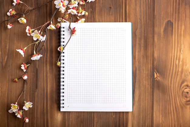 Top view open copybook with flowers on the brown desk