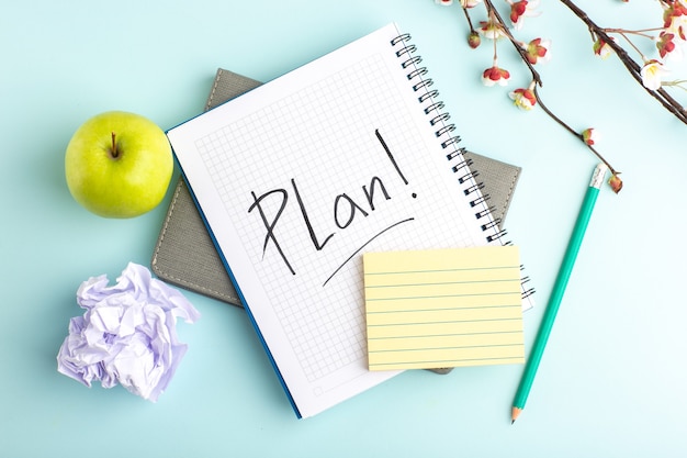 Top view open copybook with green apple and flowers on light-blue desk