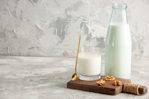 Top view of open glass bottle and cup filled with milk spoon and walnut on the left side on ice background