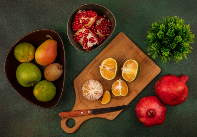 Top view of open and halved fresh tangerines on a wooden kitchen board with knife with open pomegranates on a bowl