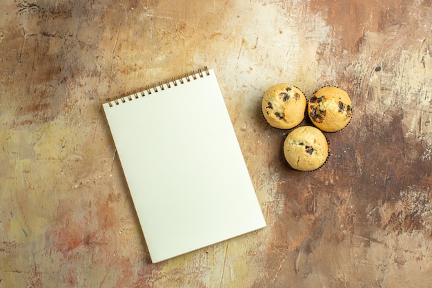 Top view of open notepad with delicious cakes on brown surface