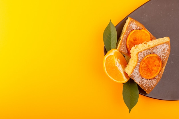 トップビューオレンジケーキスライス甘いおいしいおいしい作品茶色の木製の机と黄色の背景の甘い砂糖ビスケット