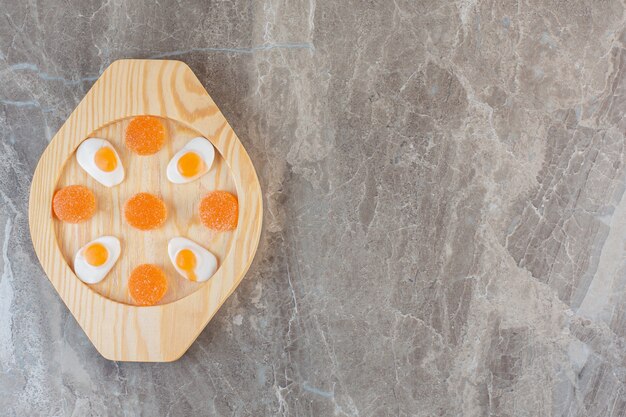 Top view of orange candies on wooden plate. 