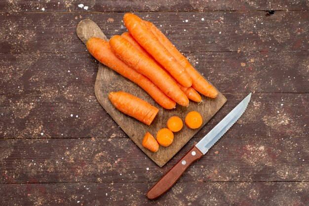 Top view orange carrots sliced and whole on brown