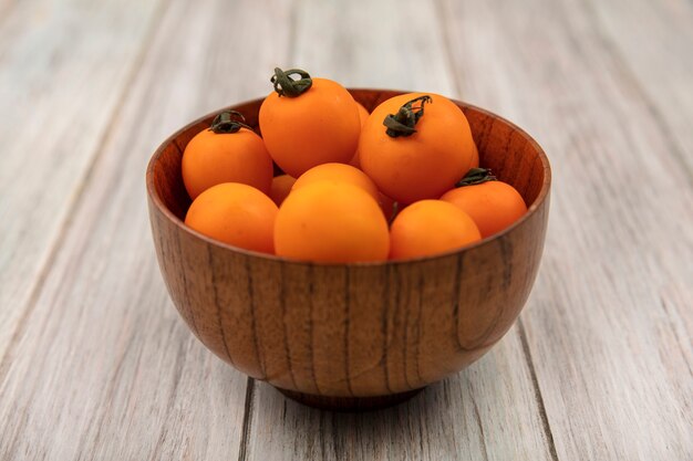 Top view of orange cherry tomatoes on a wooden bowl on a grey wooden background