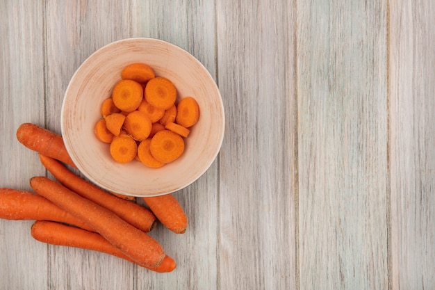Вид сверху оранжевой нарезанной моркови на миске с морковью, изолированной на серой деревянной поверхности с копией пространства