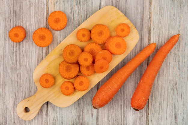 Top view of orange chopped carrots on a wooden kitchen board with carrots isolated on a grey wooden wall