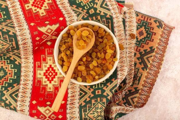 A top view orange dried raisins inside round plate on colorful designed carpet on pink