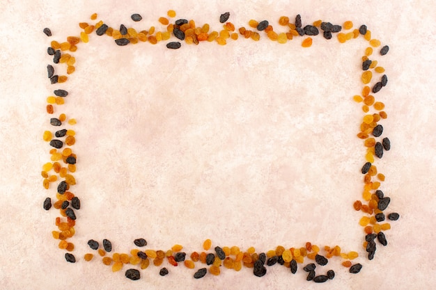 A top view orange dried raisins with black dried fruits shaping square on pink