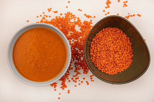 Top view of orange lentil soup on a bowl with fresh lentils on a bowl on a white wall