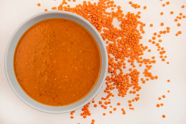Vista dall'alto di zuppa di lenticchie arancione su una ciotola con lenticchie fresche isolato su un muro bianco