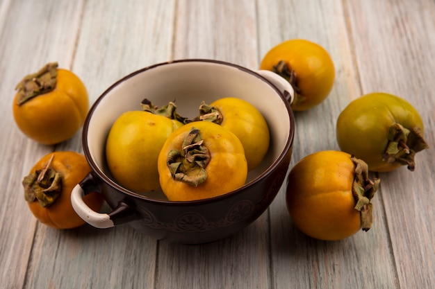 Free photo top view of orange organic persimmon fruits on a bowl on a grey wooden table