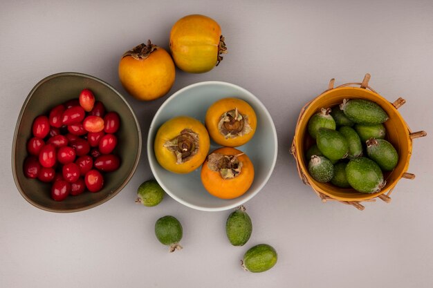 회색 벽에 그릇에 양동이에 feijoas와 산수유 체리와 그릇에 오렌지 감 과일의 상위 뷰