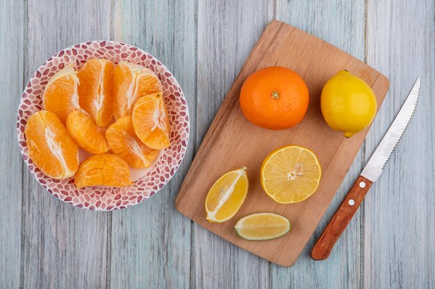 Top view orange slices on plate with lemon wedges on cutting board with knife on gray background