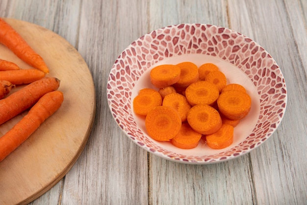 Top view of orange tasty chopped carrots on a bowl on a grey wooden wall