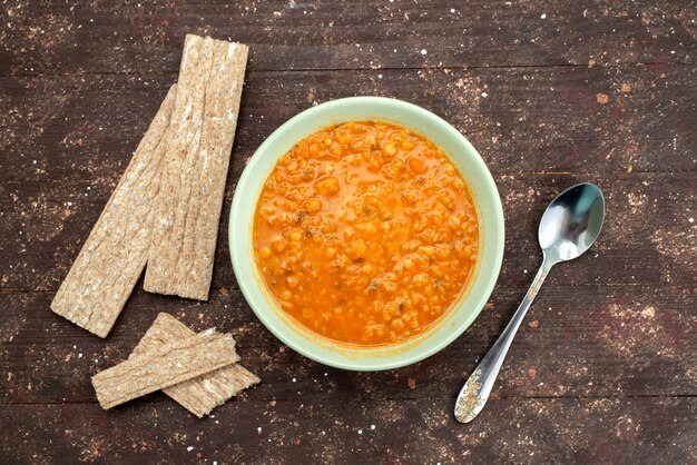 Top view orange tasty soup with crackers and spoon on brown, food meal dinner soup