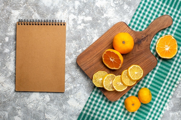 Top view oranges lemon slices on wood board lemons on green white checkered tablecloth notepad on grey table