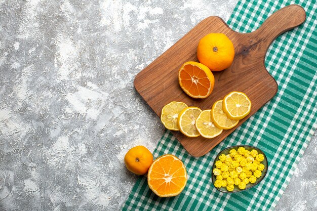 Вид сверху апельсины дольки лимона на деревянной разделочной доске лимоны на зеленой белой клетчатой скатерти на сером столе свободное пространство