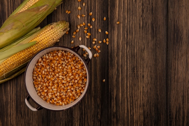 Top view of organic corn kernels on a bowl with fresh corns with hair isolated on a wooden table with copy space