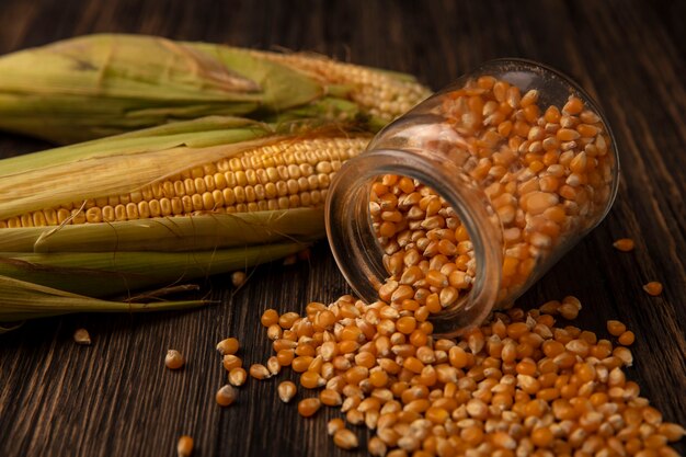 Top view of organic corn kernels falling out of a glass jar with kernels isolated on a wooden table