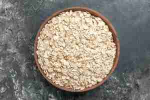 Free photo top view of organic oat bran in a brown wooden pot on dark background