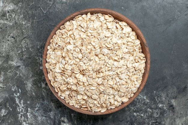 Top view of organic oat bran in a brown wooden pot on dark background
