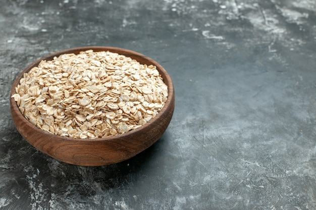 Top view of organic oat bran in a brown wooden pot on the right side on dark background