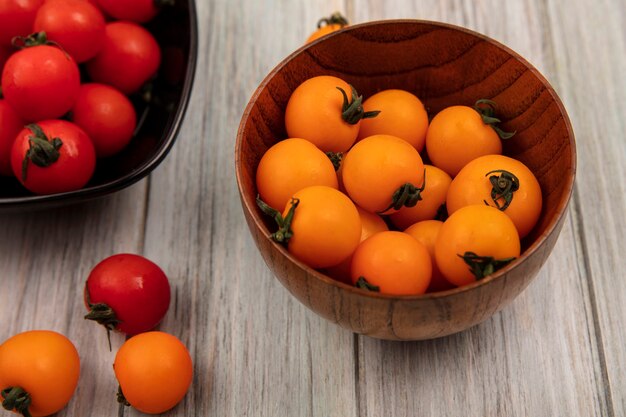 Top view of organic orange tomatoes on a wooden bowl with red tomatoes on a black bowl on a grey wooden surface