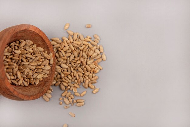Top view of organic shelled sunflower seeds falling out of a wooden bowl with copy space
