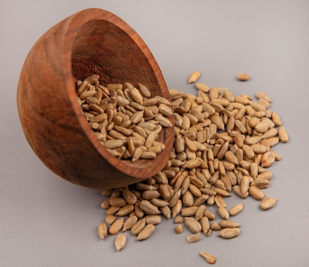 Top view of organic shelled sunflower seeds falling out of a wooden bowl